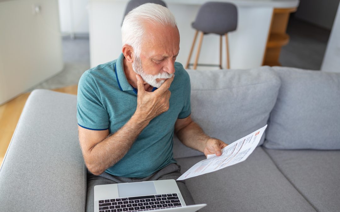 Concerned older man reading tax-related letter while seated on a sofa with a laptop, reflecting the stress of tax audits and IRS communications.